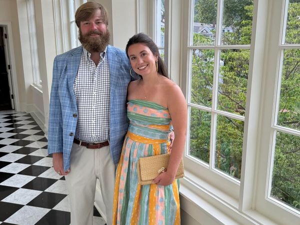 A couple dressed elegantly posing in a bright hallway with large windows.