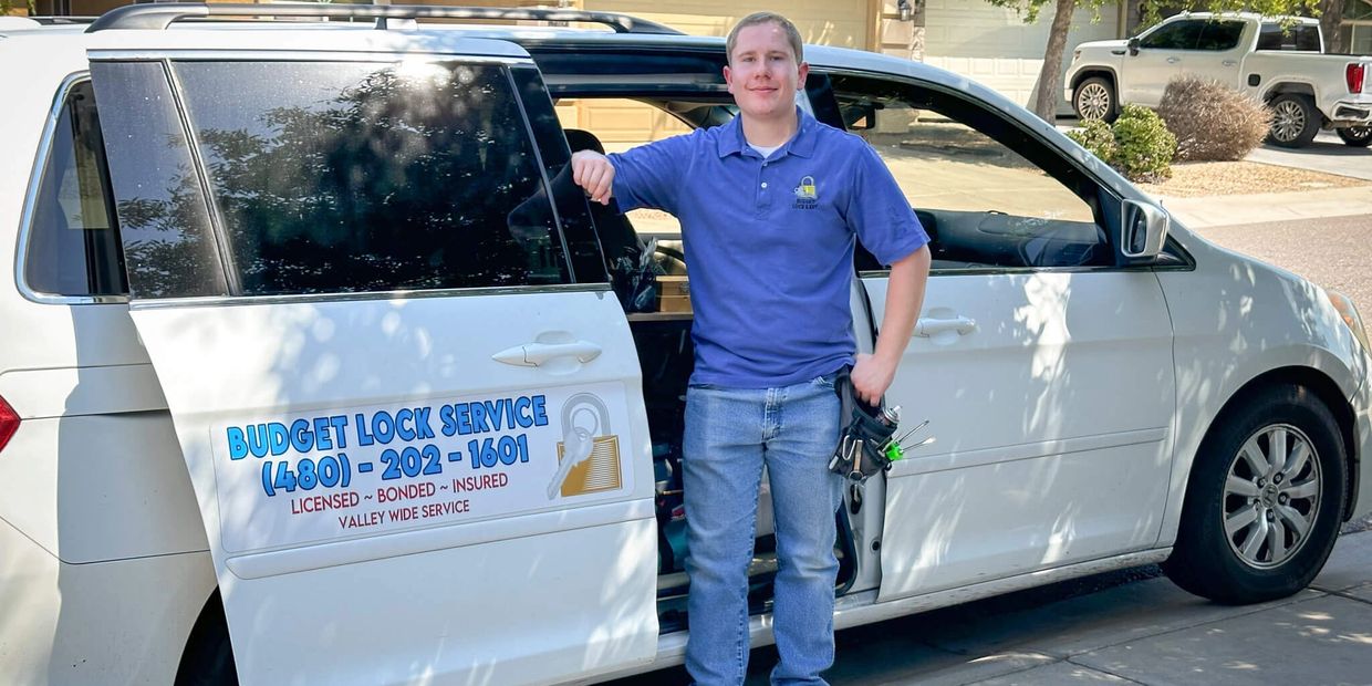 Locksmith standing by vehicle with tools and company branding.