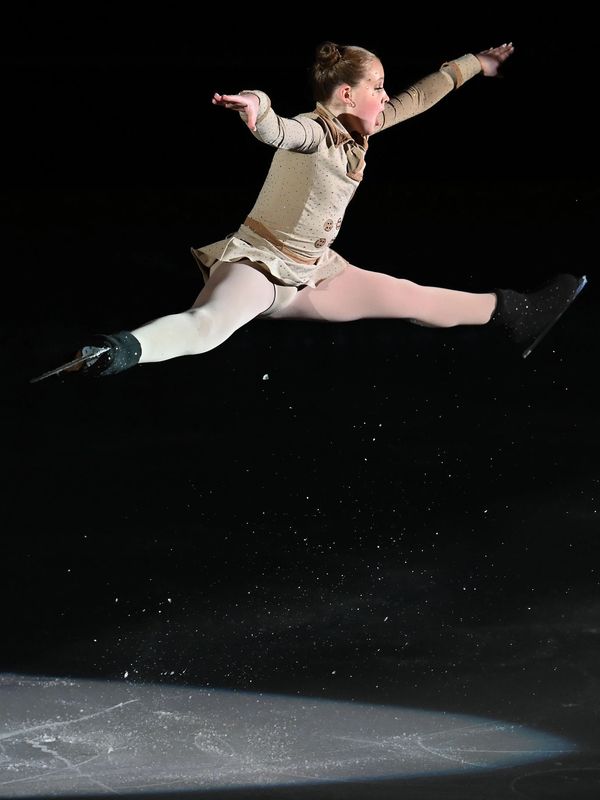 Young figure skater performing a split jump.