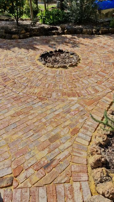 Circular recycled brick patio with a central fire pit surrounded by garden beds and a path.