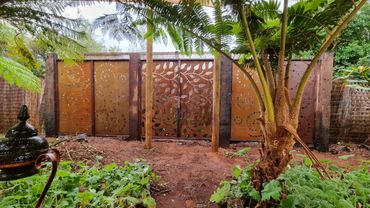 Decorative jarrah and steel garden fence with leaf and spiral patterns, surrounded by a lush shaded