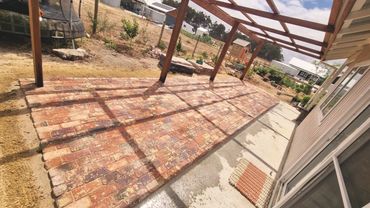 New recycled red brick patio with wooden pergola casting shadows on a sunny day.