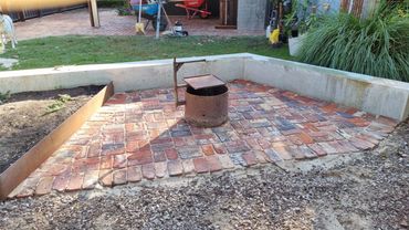 A brick patio with a metal fire pit and surrounding garden area.