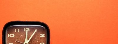 A classic analog clock showing 12:05 against an orange background.