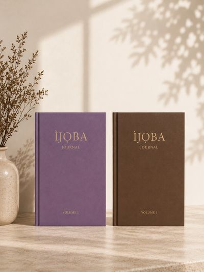 Two elegant IJQBA journals in purple and brown with a ceramic vase beside them.
