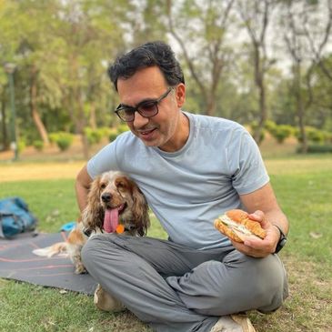 Man sitting on grass with dog and sandwich.