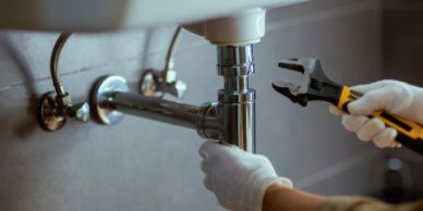 Plumber fixing a kitchen sink pipe with a wrench.
