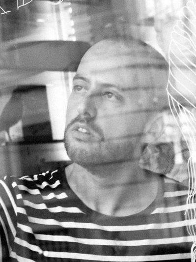 Man with beard in striped shirt looking thoughtfully through a window.