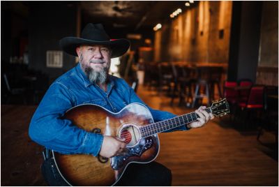 A man in a cowboy hat playing an acoustic guitar indoors.