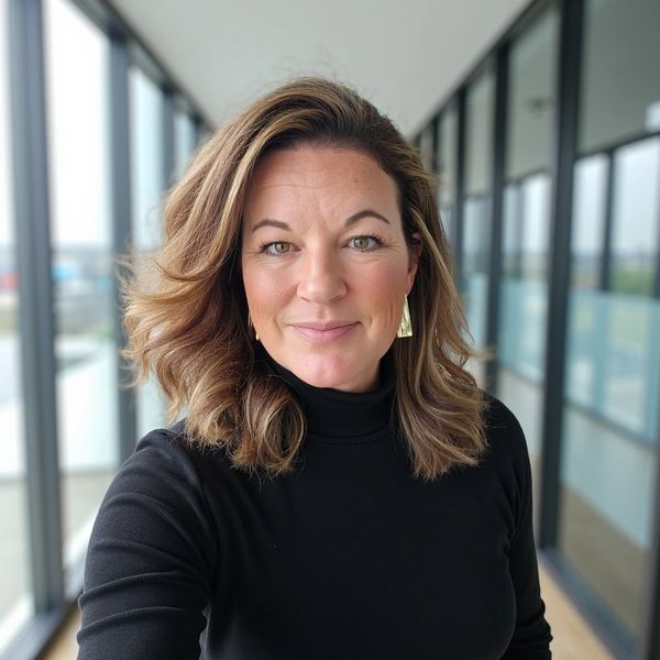 Smiling woman with wavy hair wearing a black turtleneck indoors.