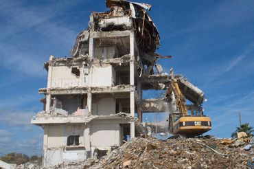 A building is being demolished by an excavator under a clear blue sky.