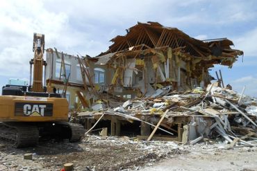 Heavy machinery demolishing a large house, leaving debris and rubble.