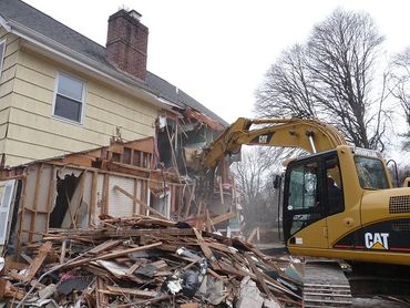Excavator demolishing a house with debris piled in front.