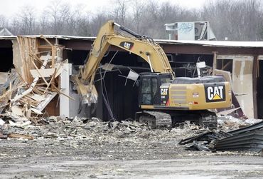 A CAT excavator demolishing a building amid rubble.