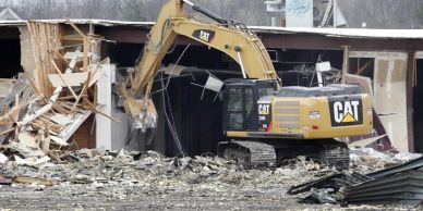 A CAT excavator demolishing a building with debris scattered around.