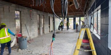 Construction workers inside a partially built space with exposed wiring and concrete walls.