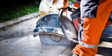 Worker cutting concrete with a circular saw on a sunny day.