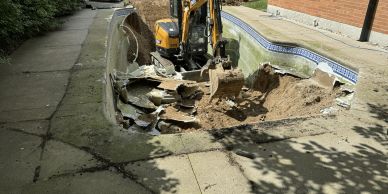Mini excavator demolishing an old in-ground pool in a backyard.