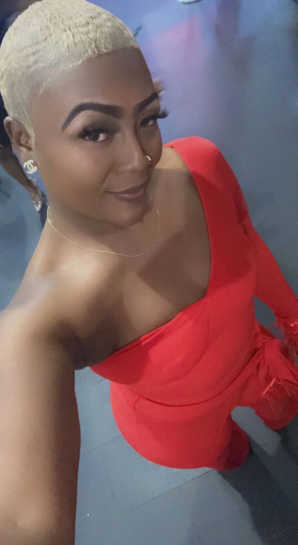 Woman with blonde hair in a red one-shoulder outfit taking a selfie.