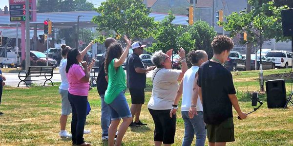 People standing and waving outdoors on a sunny day.