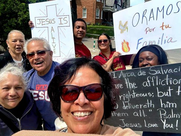 Group holding religious signs with smiles in a sunny outdoor setting.