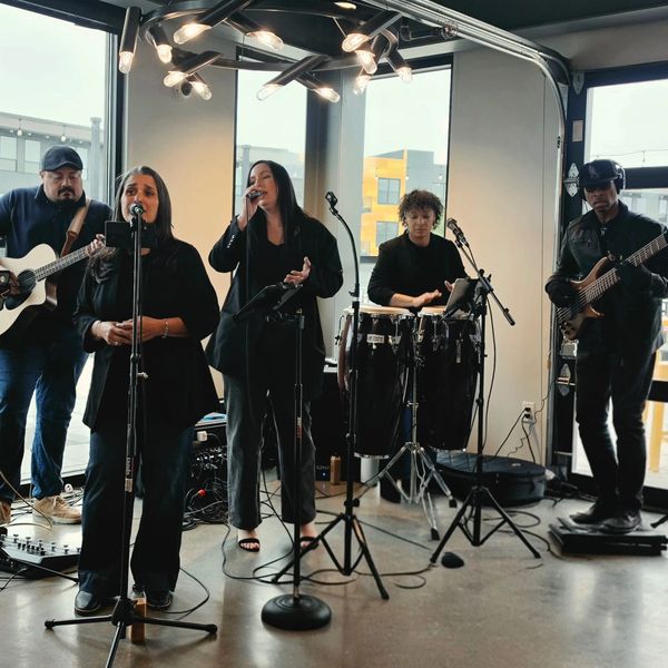 Band performing indoors with microphones and instruments.