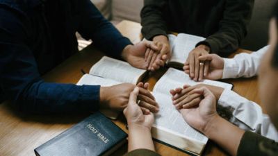 People holding hands in prayer over open Bibles.