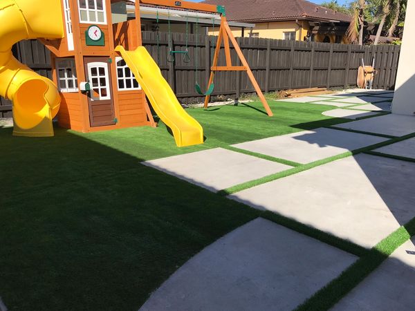 Artificial grass strips between concrete slabs in backyard playround