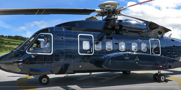 A sleek black helicopter parked on a helipad under a blue sky.
