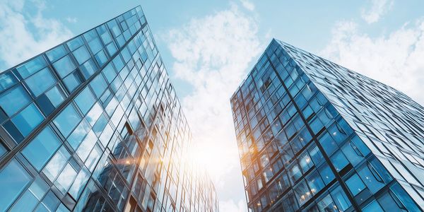 Sunlight shines between two modern glass skyscrapers under a blue sky.