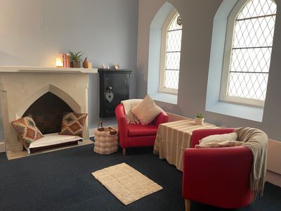 Warm space containing two armchairs, cushions and a rug in a room with two tall windows.