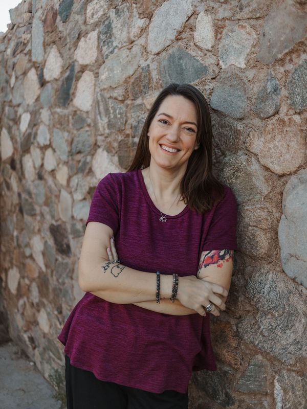 Smiling woman in purple shirt leaning against a stone wall.