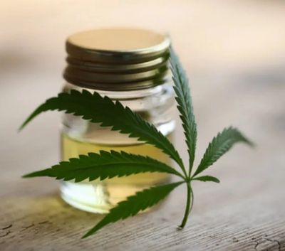 A cannabis leaf next to a small jar of cannabis oil on a wooden surface.