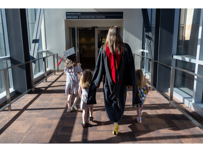 Graduate walking with three young children in an indoor walkway.