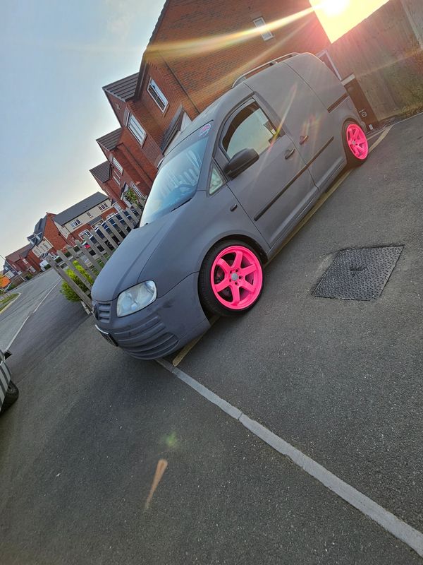 Grey van with bright pink wheels parked on street at sunset.