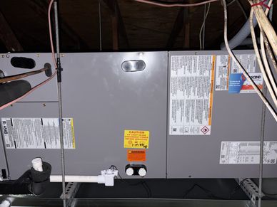 Industrial HVAC unit mounted in a ceiling space with warning labels and pipes.