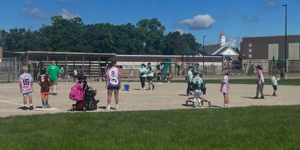 Children and adults playing baseball on a sunny day.