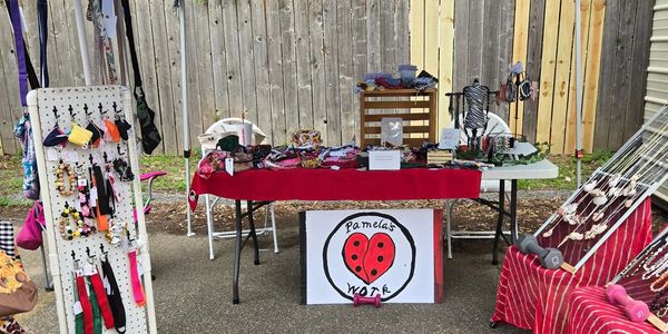 A booth at a Farmer's market. The display includes a coatrack with tote bags hanging on it and table