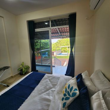 Cozy bedroom with blue accents and a balcony view of greenery and a pool.