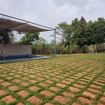 Outdoor area with patterned grass, a small pool, and a swing set surrounded by trees.
