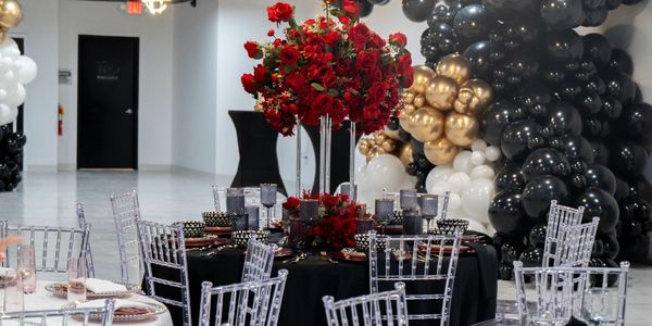 Elegant black and gold themed event table with red floral centerpiece and clear chairs.