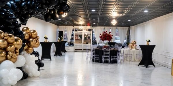 Elegant event space with black, gold, and white balloon decor and chic table settings.