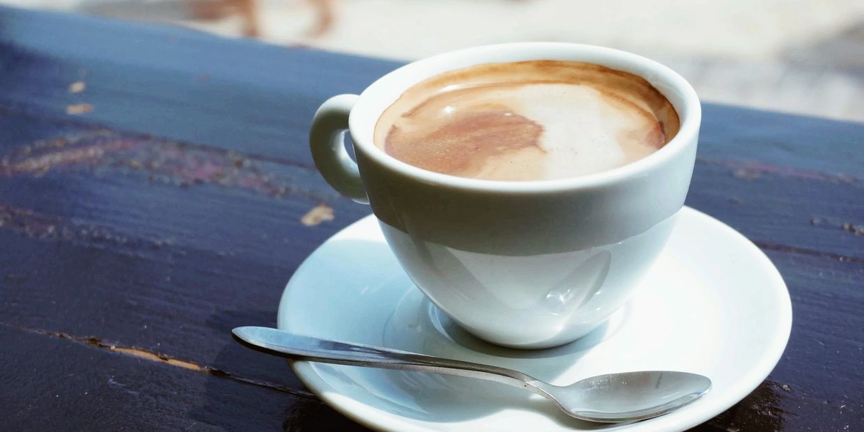 A cup of coffee with a spoon on a saucer on a wooden table.