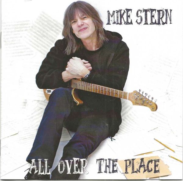 Mike Stern holding a guitar, smiling.