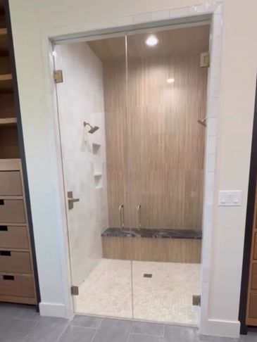 Modern glass shower with wooden accent wall and built-in bench.