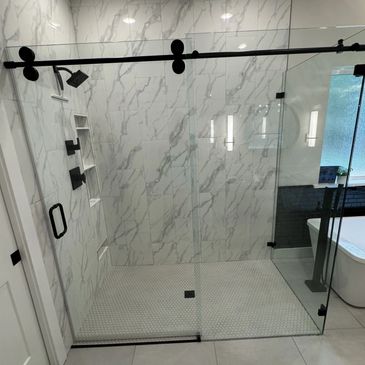 Modern walk-in shower with marble tiles and black fixtures.