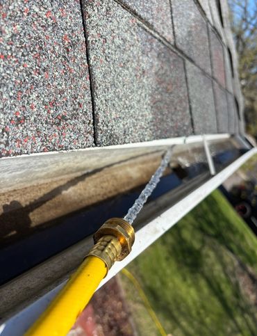 Using a hose to flush out gutters on a residential home after a gutter cleaning