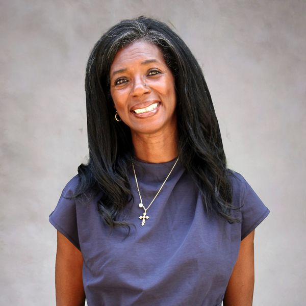 Smiling woman with long black hair and cross necklace.