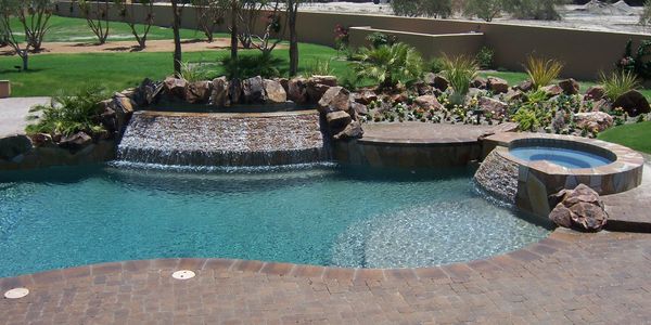 Elegant backyard pool with waterfall and spa surrounded by lush greenery.