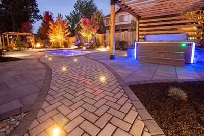 Illuminated backyard path leading to a hot tub and small pool at night.